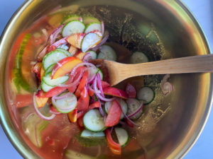 Combining the peaches, tomatoes, cucumber and onions with the vinaigrette