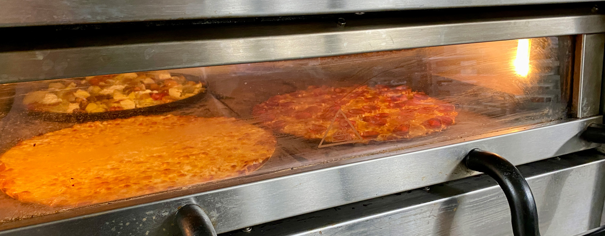 Two Foreground Pizzas Doing Final Bake Directly on the Stone