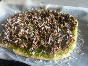 Pesto, sausage and cheese layered on fir the first bake